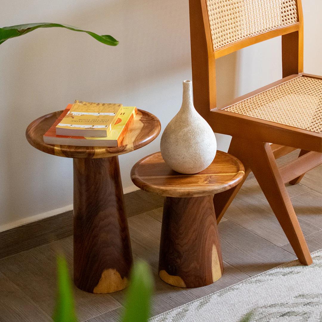 Wooden side table with books and a vase, next to a wicker chair.